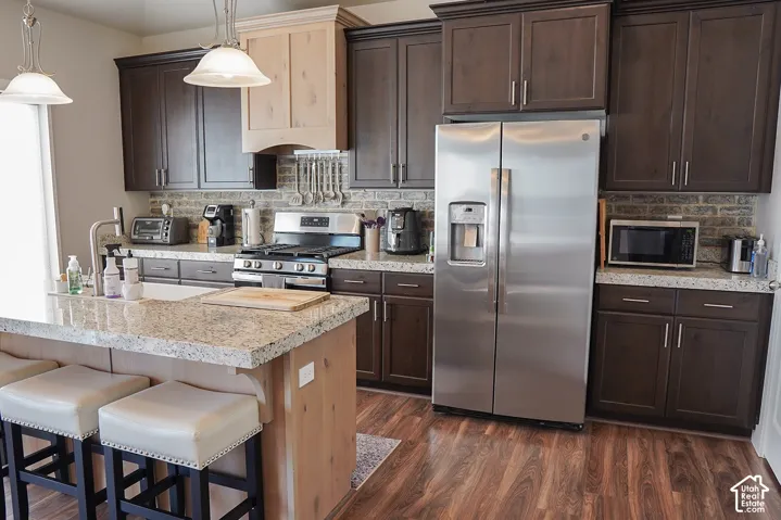 Kitchen featuring a granite-finish island, wood-finish flooring, two-tone cabinetry, a stainless steel refrigerator, and a gas range