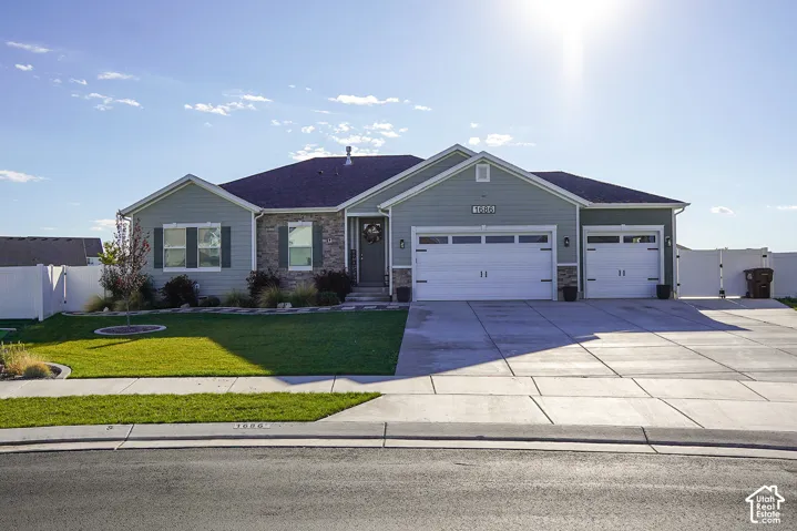 Light blue siding exterior with stone accents, two-car garage, single-car garage, concrete driveway, and a front lawn