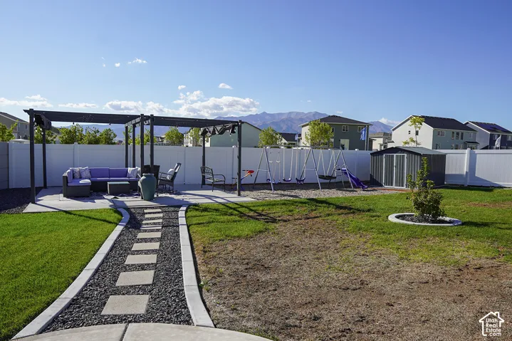 Backyard featuring a concrete patio with pergola, white vinyl fencing, a metal storage shed, and a stone-lined pathway