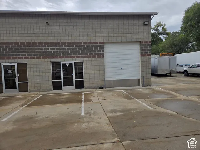Brick and concrete block exterior featuring two glass entry doors, a roll-up garage door, and a concrete parking area