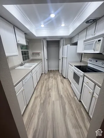 Galley kitchen featuring white cabinetry, light-toned countertops, and wood-finish flooring