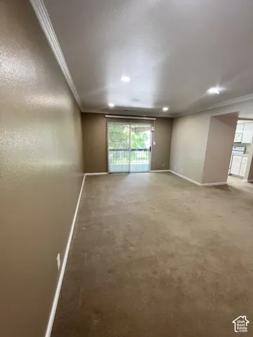 Recessed lighting illuminates the carpeted flooring and crown molding