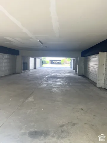 Covered parking area with concrete flooring, fluorescent lighting, and multiple enclosed storage units
