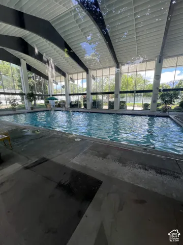Indoor swimming pool with an expansive glass enclosure, exposed structural beams, and a concrete deck