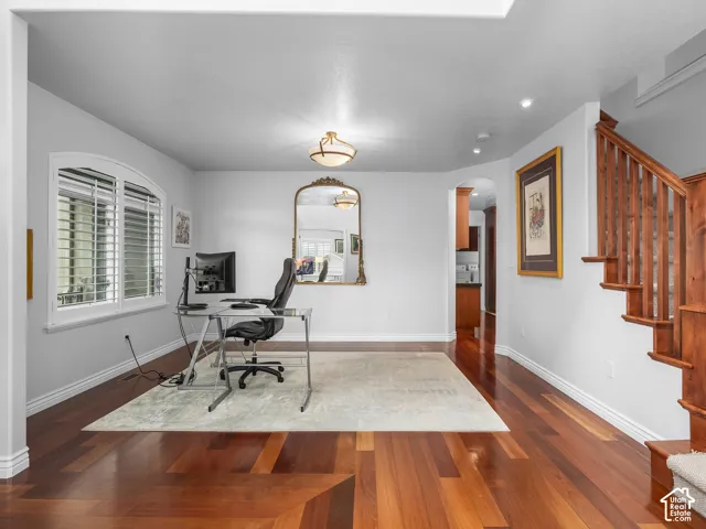 Hardwood flooring with a geometric inlay, arched window with plantation shutters, recessed lighting, and a wood staircase