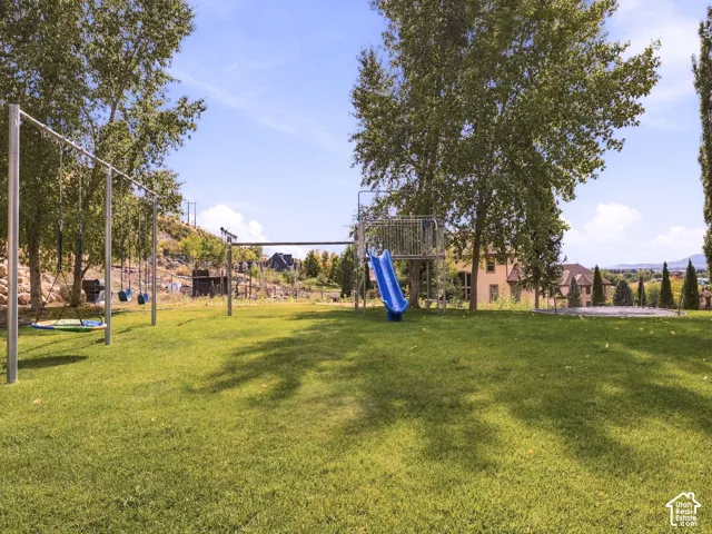 Expansive grassy area featuring a swing set, playground slide, and mature trees