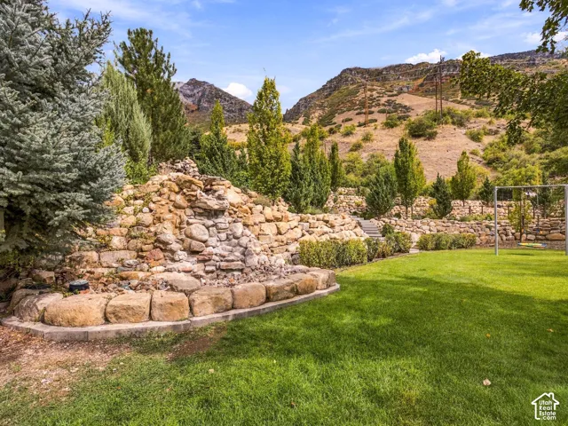 Expansive backyard featuring a manicured lawn, tiered landscaping with stone retaining walls, and mature trees