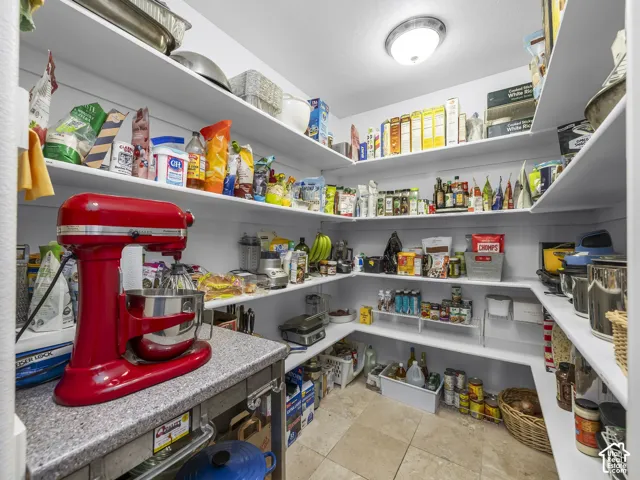 Walk-in pantry with extensive built-in shelving, stone-finish countertop, and tiled flooring