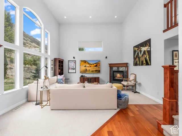 Soaring ceilings with upper windows, expansive window wall, fireplace with wood surround, wood-finish flooring, and a carpeted living area
