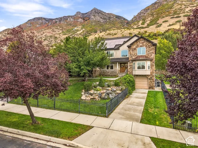 Stone-clad exterior, bay window, solar panels, attached garage, and mature landscaping