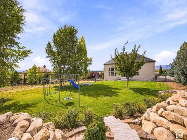 Expansive lawn featuring a swing set with a slide, mature trees, and a stone retaining wall