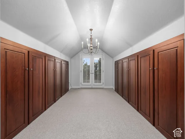 Vaulted ceiling, built-in wood-finish cabinetry, chandelier, light-colored carpeting, and French doors with privacy shutters