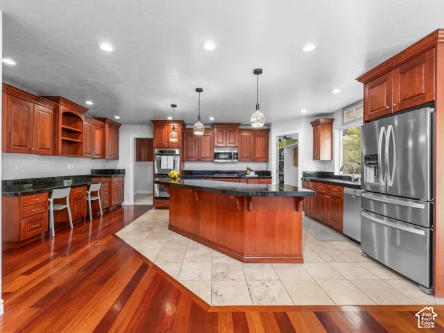Kitchen featuring rich wood cabinetry, dark countertops, a central island, recessed lighting, and stainless steel appliances