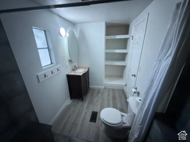 Bathroom featuring wood-finish flooring, a single window, built-in shelving, a dark wood-finish vanity with a light-colored countertop, and an oval mirror