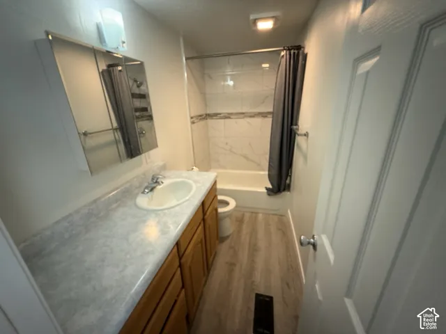 Bathroom featuring a white vanity with an integrated sink, wood-finish cabinetry, a large mirrored medicine cabinet, a bathtub with a tiled surround, and wood-finish flooring