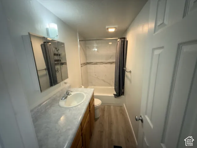 Wood-finish flooring, light-toned countertop, wood vanity cabinetry, mirrored medicine cabinet, and white subway tile bath surround with decorative accent