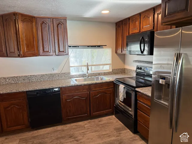 Kitchen featuring wood-finish cabinetry, granite-finish countertops, stainless steel refrigerator, built-in microwave, and wood-finish flooring