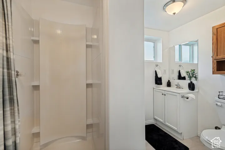 Basement bathroom featuring white vanity with a single basin sink, wall-mounted mirror, and shower surround.