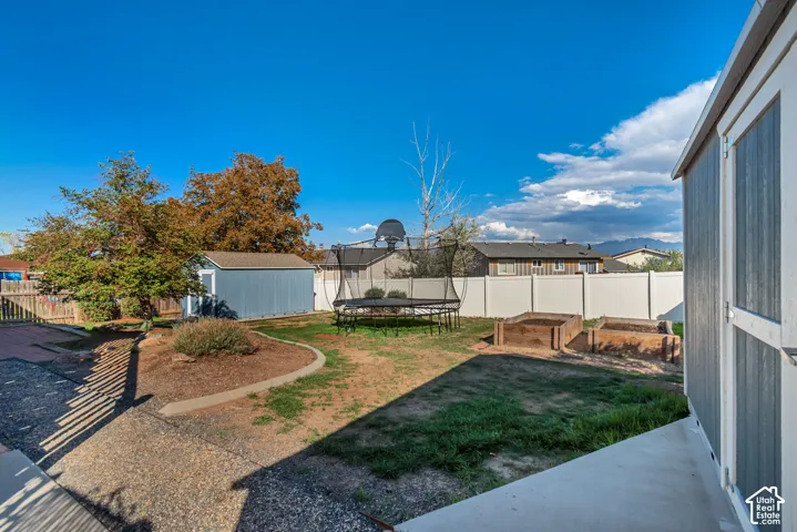 Expansive backyard with a paved patio, gravel path, raised garden beds, and a perimeter privacy fence