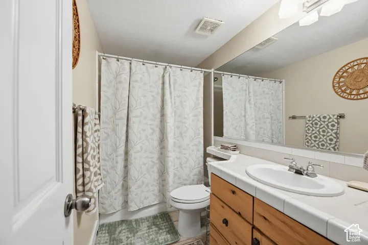 Built-in vanity with wood-finish cabinetry, tile countertop, and integrated sink