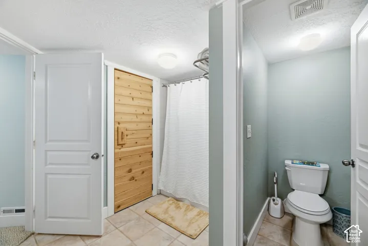 Tile flooring, wood-paneled door, shower with white curtain, toilet with white finish, flush-mount ceiling lighting