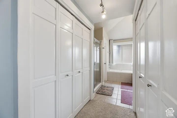 Vaulted ceiling bathroom featuring a built-in tub, tiled floor, glass-enclosed shower, and track lighting