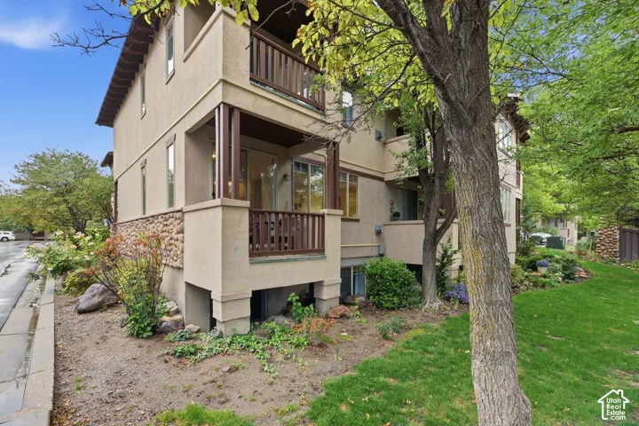 Stucco exterior with stone accent detailing, private balconies with wood railings, mature landscaping, and an adjacent grassy area