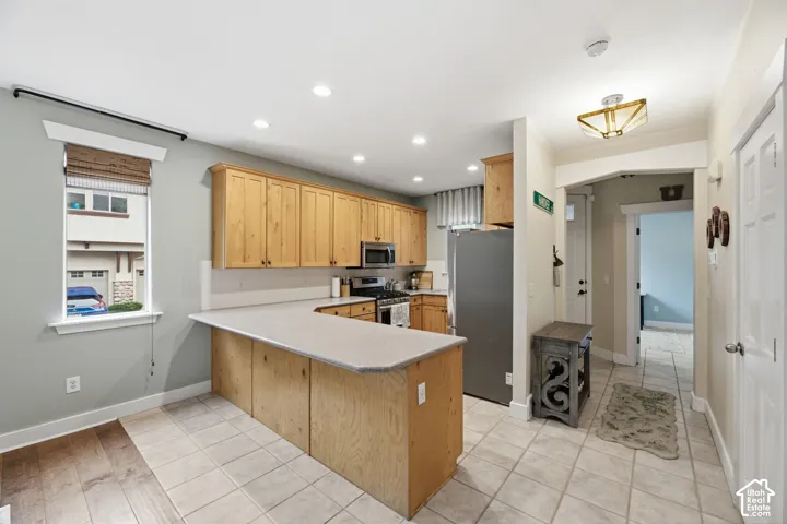 Kitchen featuring light wood cabinetry, stainless steel appliances, recessed lighting, and a window with a woven shade