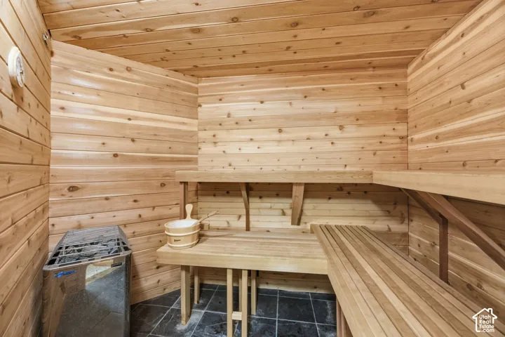 Interior sauna featuring wood paneling, built-in wooden benches, and dark stone-look flooring