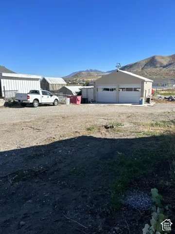 Detached two-bay garage with overhead doors, mountain backdrop, and multiple ancillary structures
