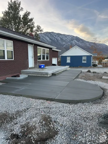 Expansive concrete patio and walkway, extending from a brick-clad home with multiple windows, all set against a prominent mountain backdrop