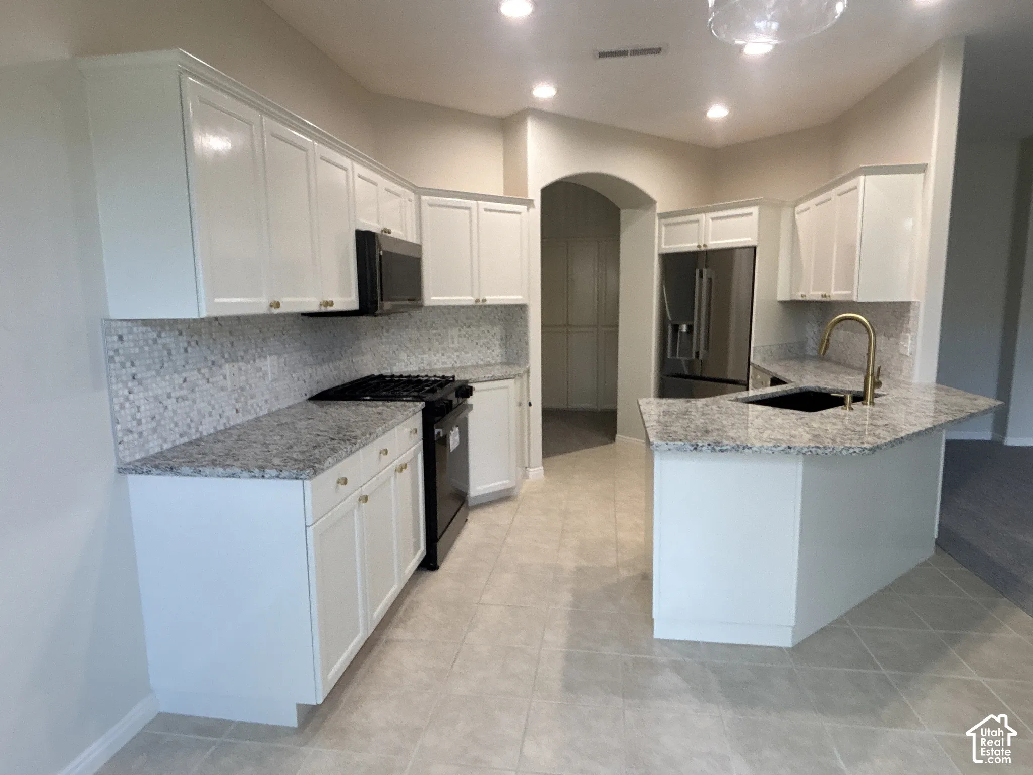 White cabinetry with gold-tone hardware, granite countertops, mosaic tile backsplash, recessed lighting, and a stainless steel refrigerator