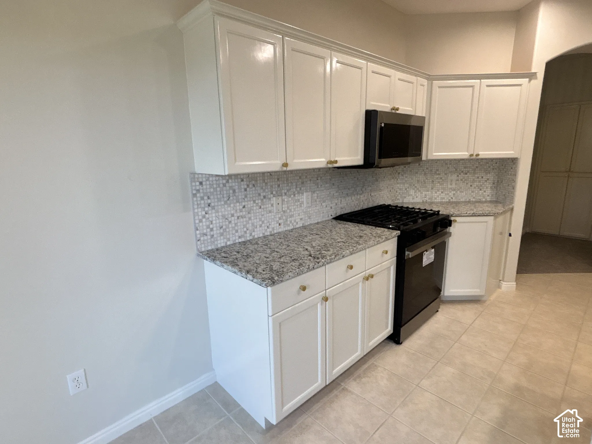 White cabinetry with gold-tone hardware, speckled countertops, mosaic tile backsplash, stainless steel range, and tile flooring