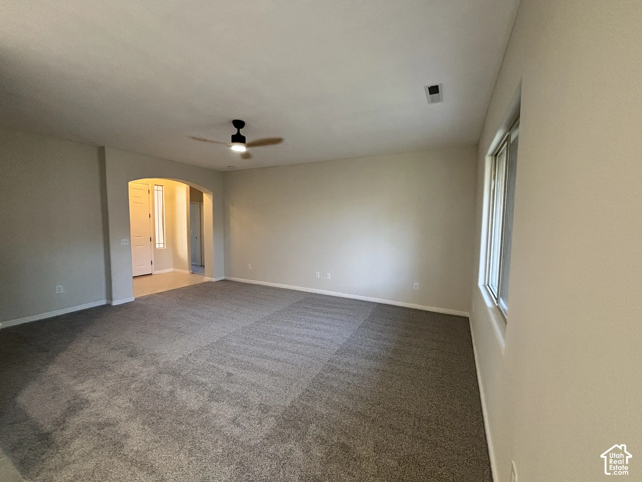 Arched entryway, neutral wall tones, window with natural light, ceiling fan with light fixture, and textured carpeting