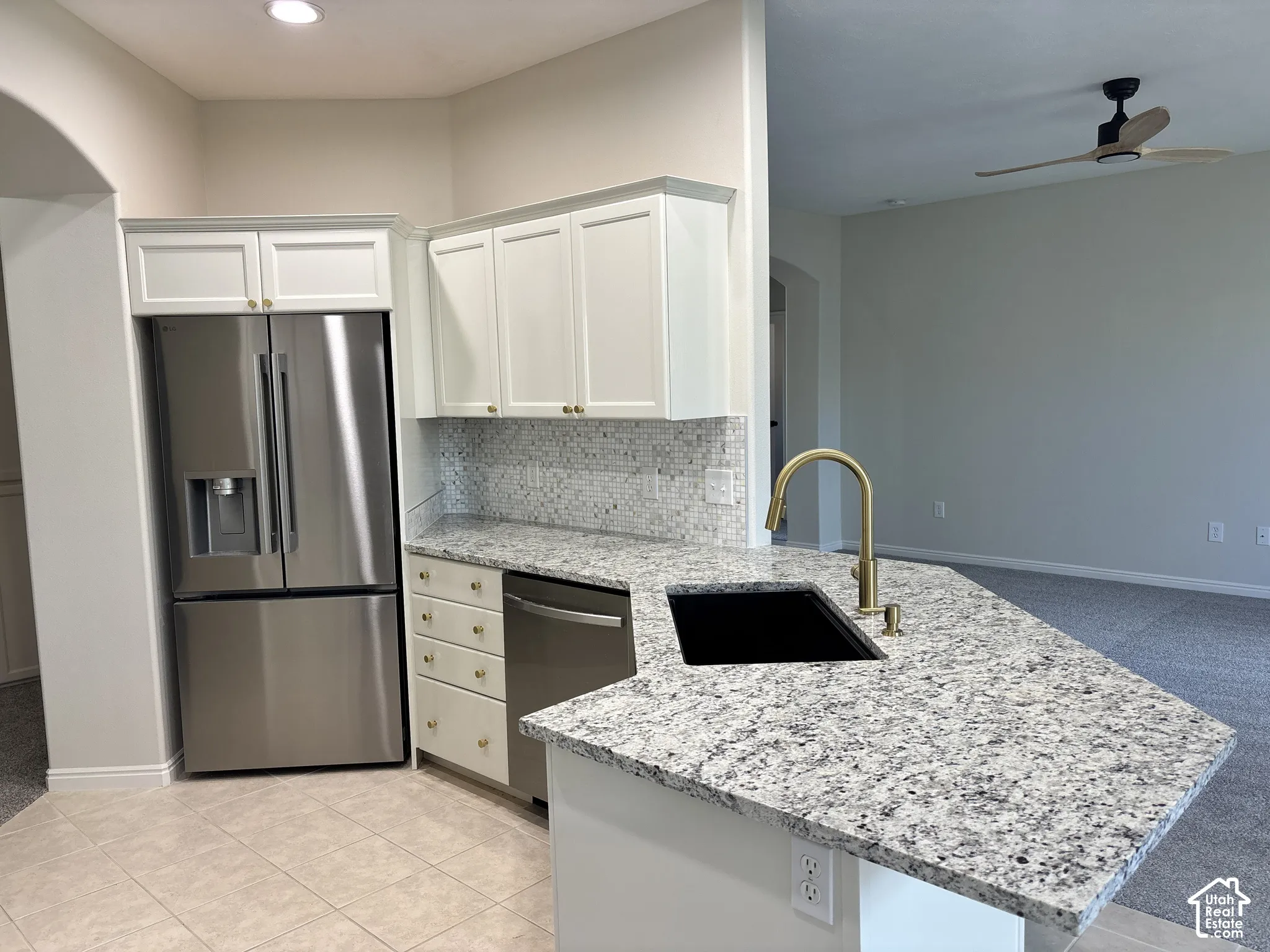 Kitchen featuring a stainless steel refrigerator, white cabinetry, granite countertops, and a tile backsplash