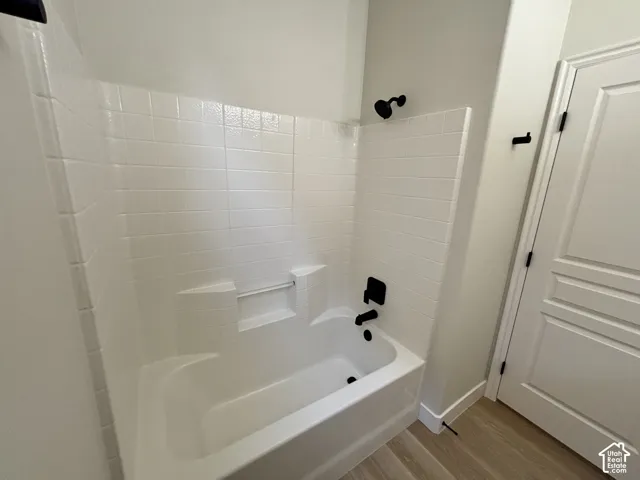 White subway tile surround with a built-in tub, matte black fixtures, and wood-finish flooring