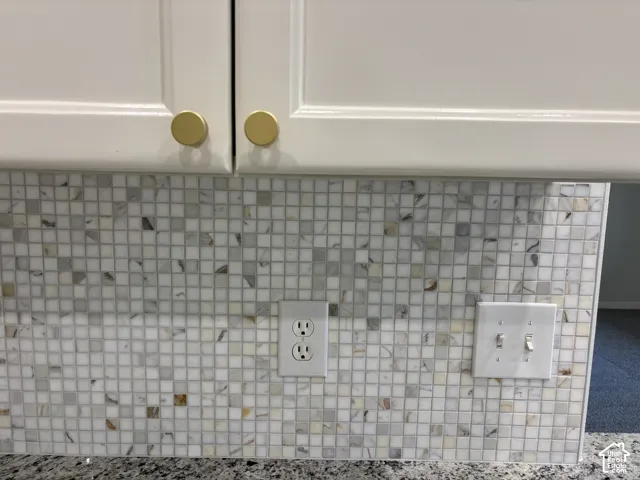 White shaker-style cabinetry with gold-tone hardware, mosaic tile backsplash, and speckled countertop