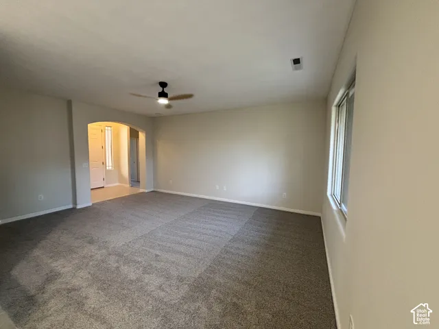 Arched entryway, neutral wall tones, window with natural light, ceiling fan with light fixture, and textured carpeting