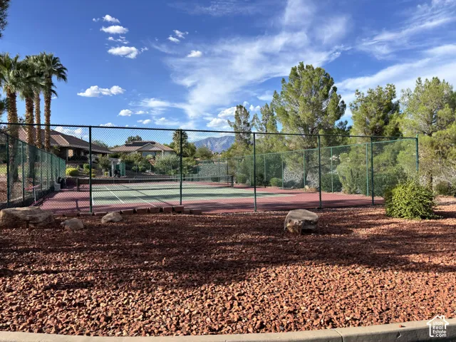 Tennis court with perimeter fencing, surrounded by xeriscaped landscaping featuring red rock and palm trees