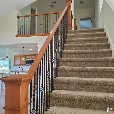 Staircase with carpeted treads, wood handrail, and decorative metal balusters