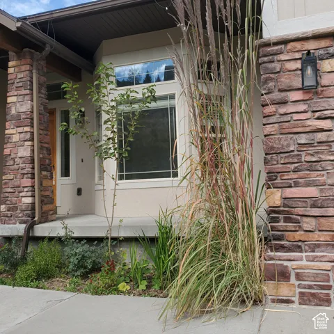 Stone veneer accents on the facade, stucco exterior finish, bay window with decorative grilles, concrete pathway, and a covered entry