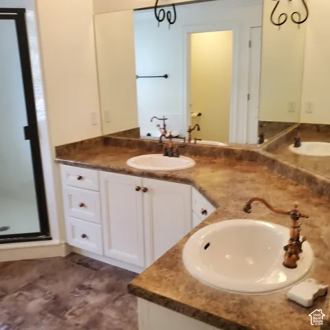 Dual vanity with integrated sinks, white cabinetry, decorative bronze-finish faucets, expansive mirror, and wood-finish flooring
