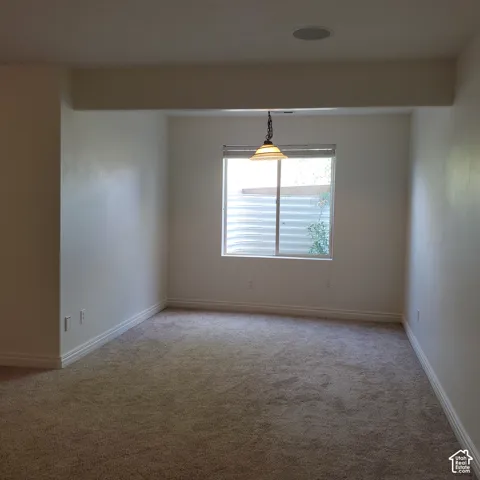 Recessed ceiling speaker, overhead pendant lighting, window with exterior well, light-toned carpet, and white baseboards