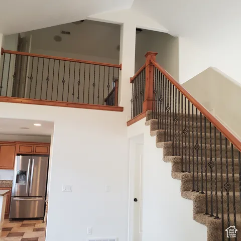 Vaulted ceiling with a carpeted staircase featuring an ornamental wrought iron and wood-finish railing