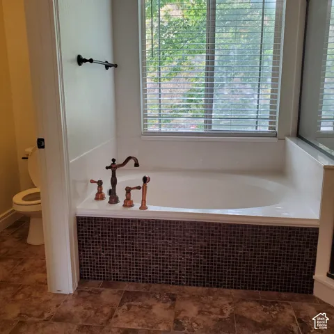 Soaking tub with bronze fixtures, mosaic tile surround, and a large window