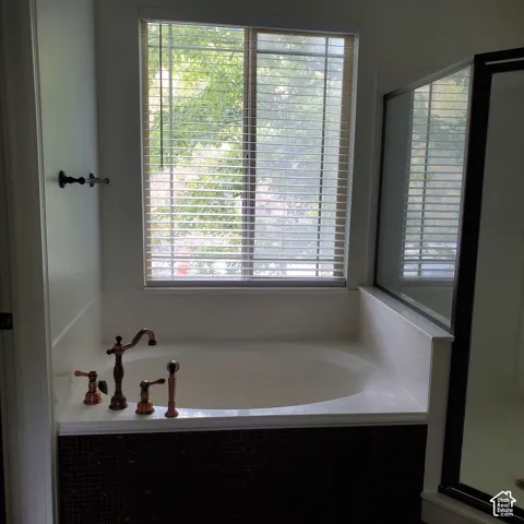Built-in soaking tub with decorative bronze-finish fixtures, a tiled surround, and an adjacent glass-enclosed shower