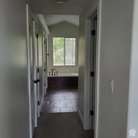 Vaulted ceiling with window, built-in soaking tub, mosaic tile tub surround, and tile flooring