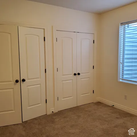 Carpeted room featuring multiple doors with paneled designs and dark hardware, window with horizontal blinds, and light-colored walls