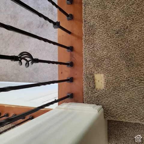 Iron balusters with decorative scrollwork, wood-finish stair treads, and neutral carpeting