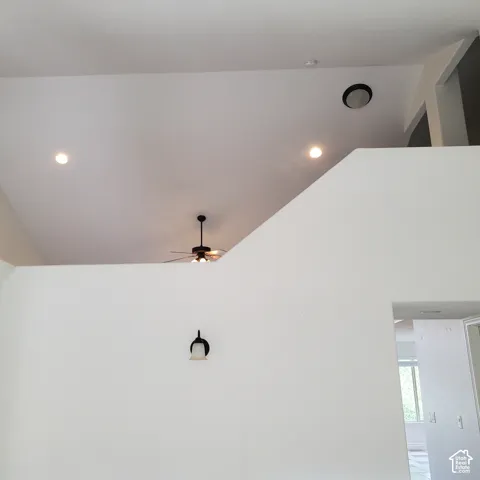 Vaulted ceiling with recessed lighting, ceiling fan, and wall-mounted sconce